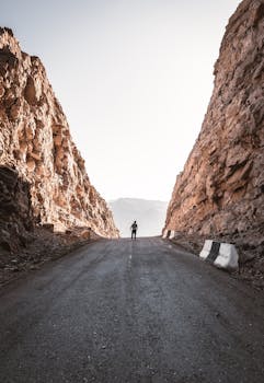 一个孤独的人行走在岩石悬崖间的荒凉山路上，开启一段冒险之旅