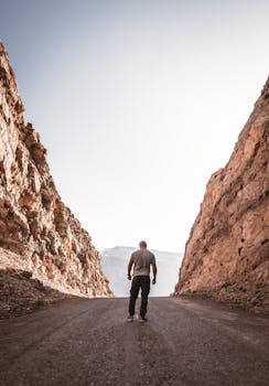 在晴朗的天空下，一名男子站在乡村道路上，两旁是高耸的岩石悬崖