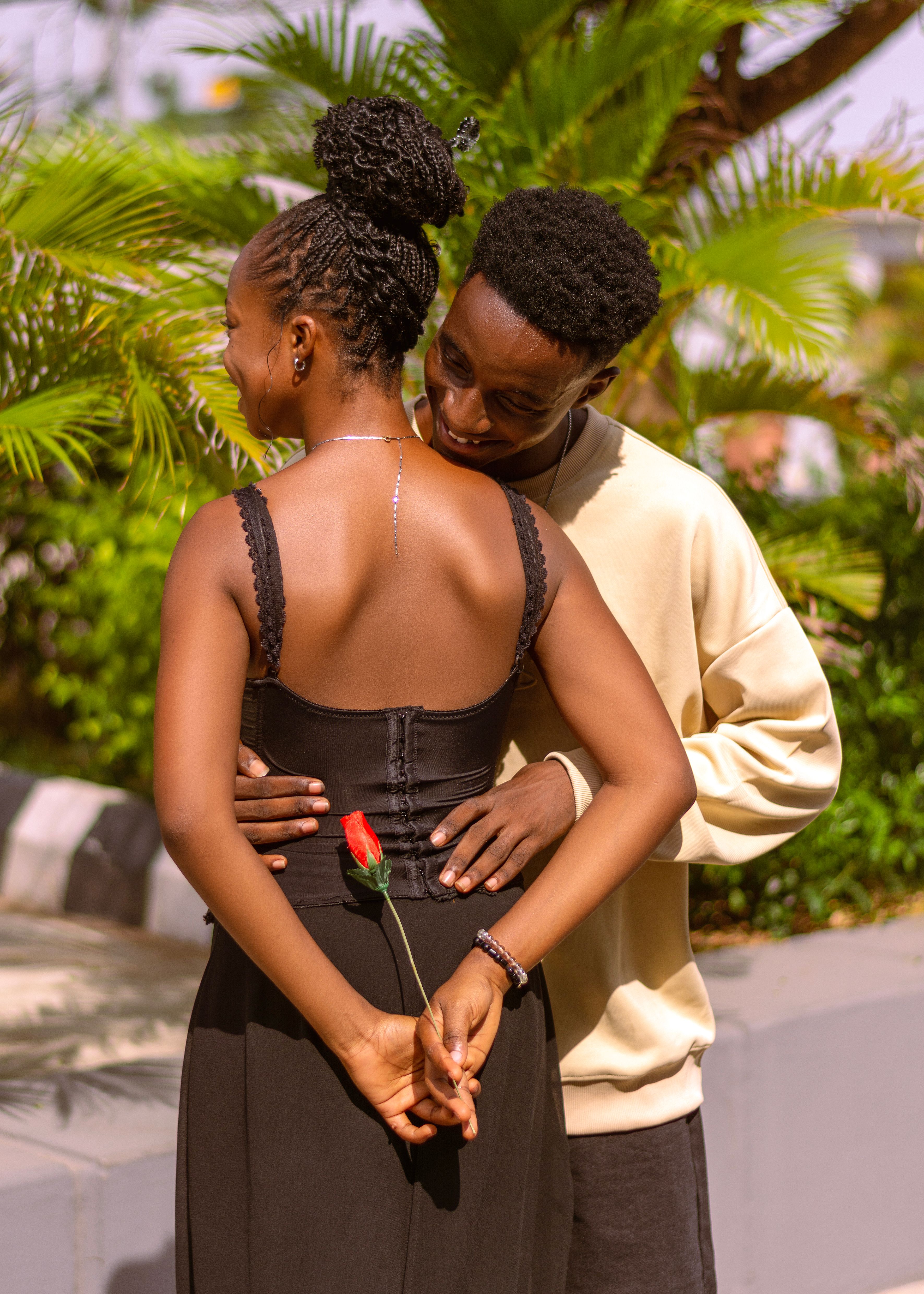 A loving couple shares a tender moment outdoors, with a red rose symbolizing romance.
