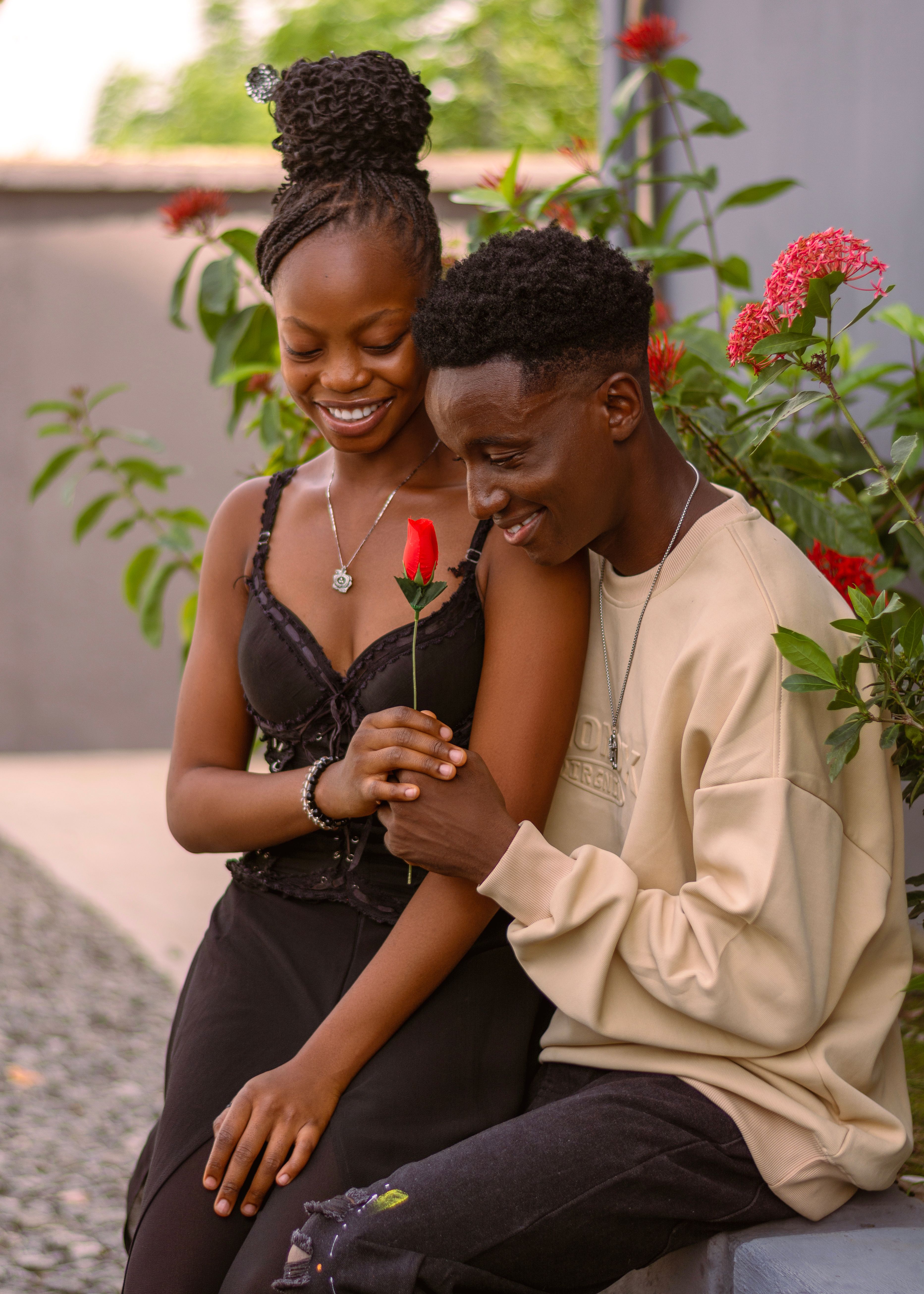 A joyful couple sharing a romantic moment with a red rose in a serene garden setting.
