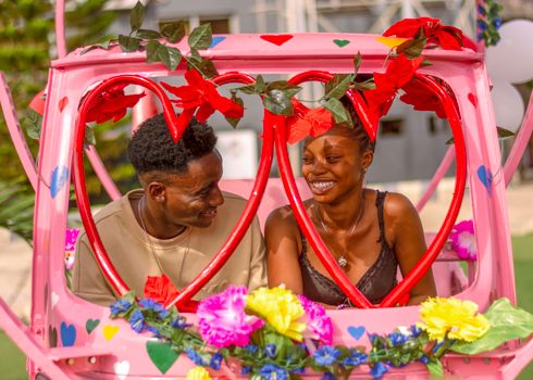 Smiling couple enjoying a ride in a colorful and heart-decorated vehicle on a sunny day.