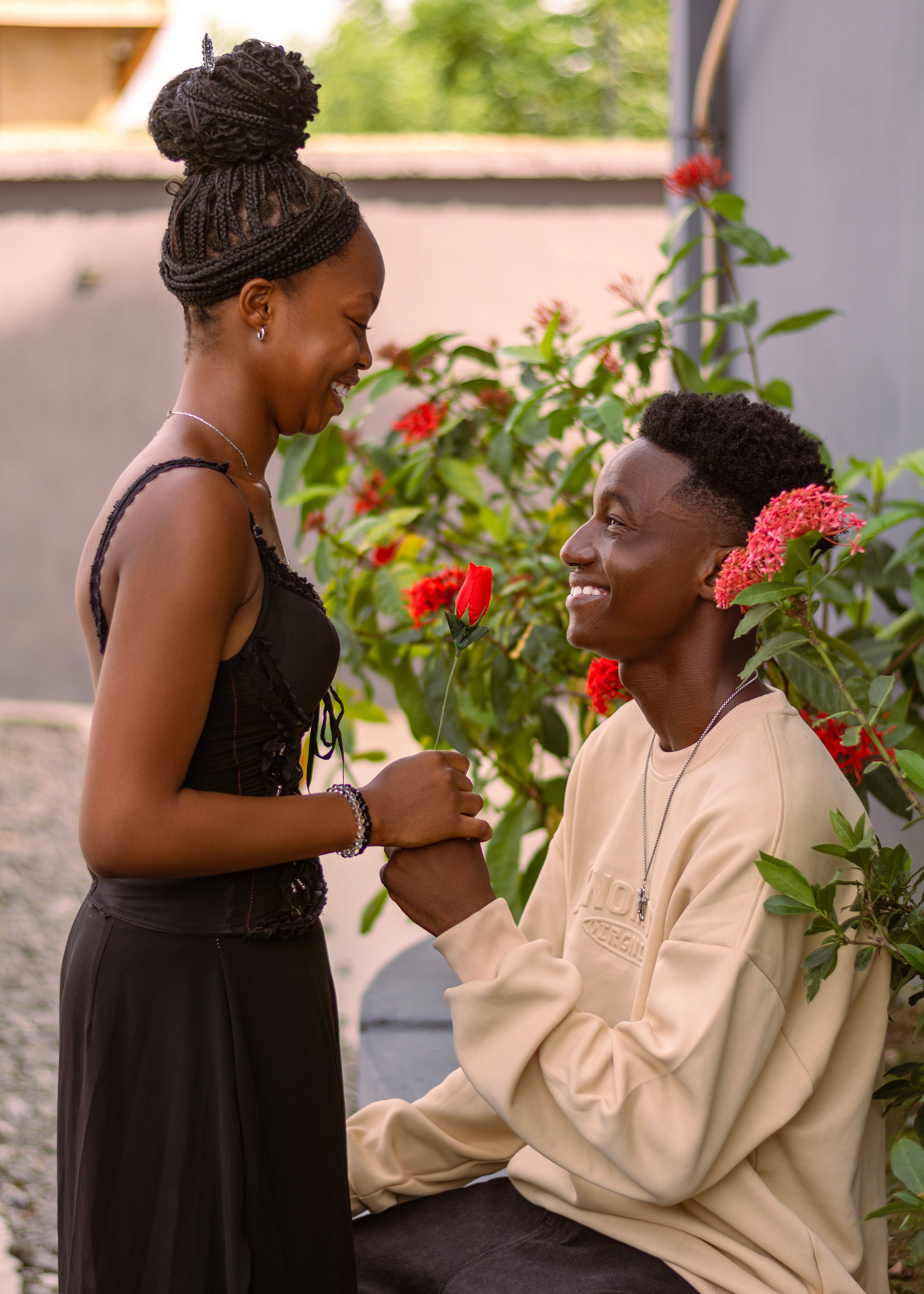 A joyful couple expresses love in an outdoor romantic setting surrounded by vibrant red flowers.