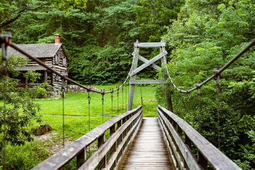 Free Charming wooden bridge leading to a quaint cabin surrounded by lush greenery in Fort Valley, Virginia. Stock Photo