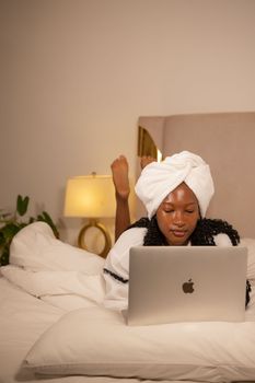 A woman in a cozy bedroom setting using a laptop, enjoying leisure time.