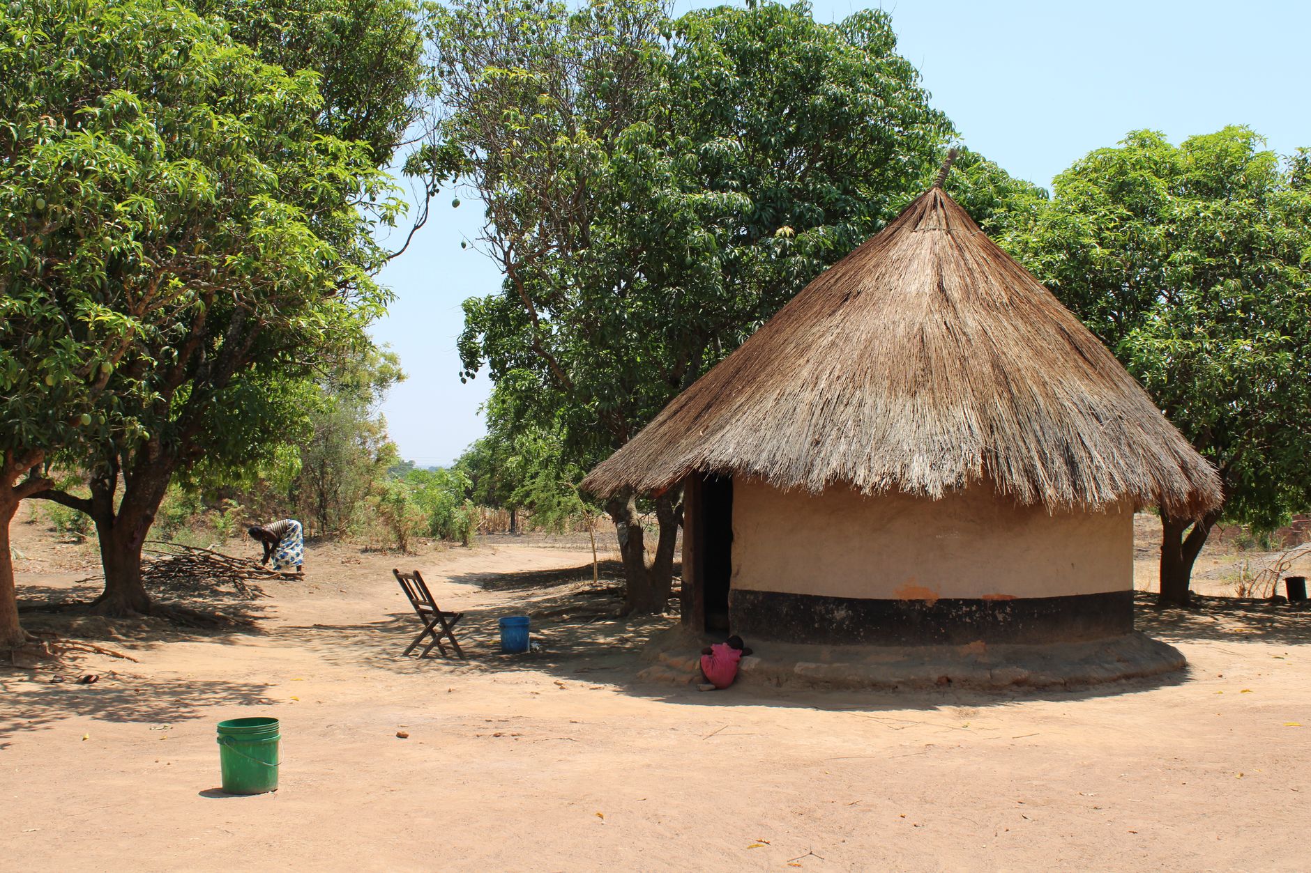 A serene view of a hut in a rural Zambian village surrounded by trees and natural landscape.