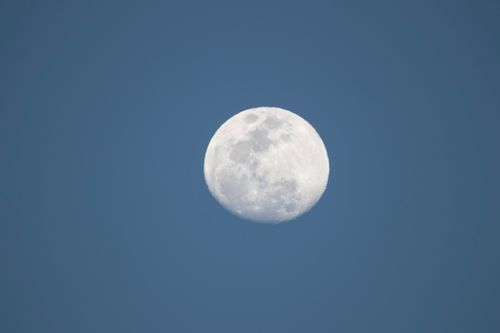 Free Close-up of the full moon visible in a bright blue sky. Captured in daylight. Stock Photo