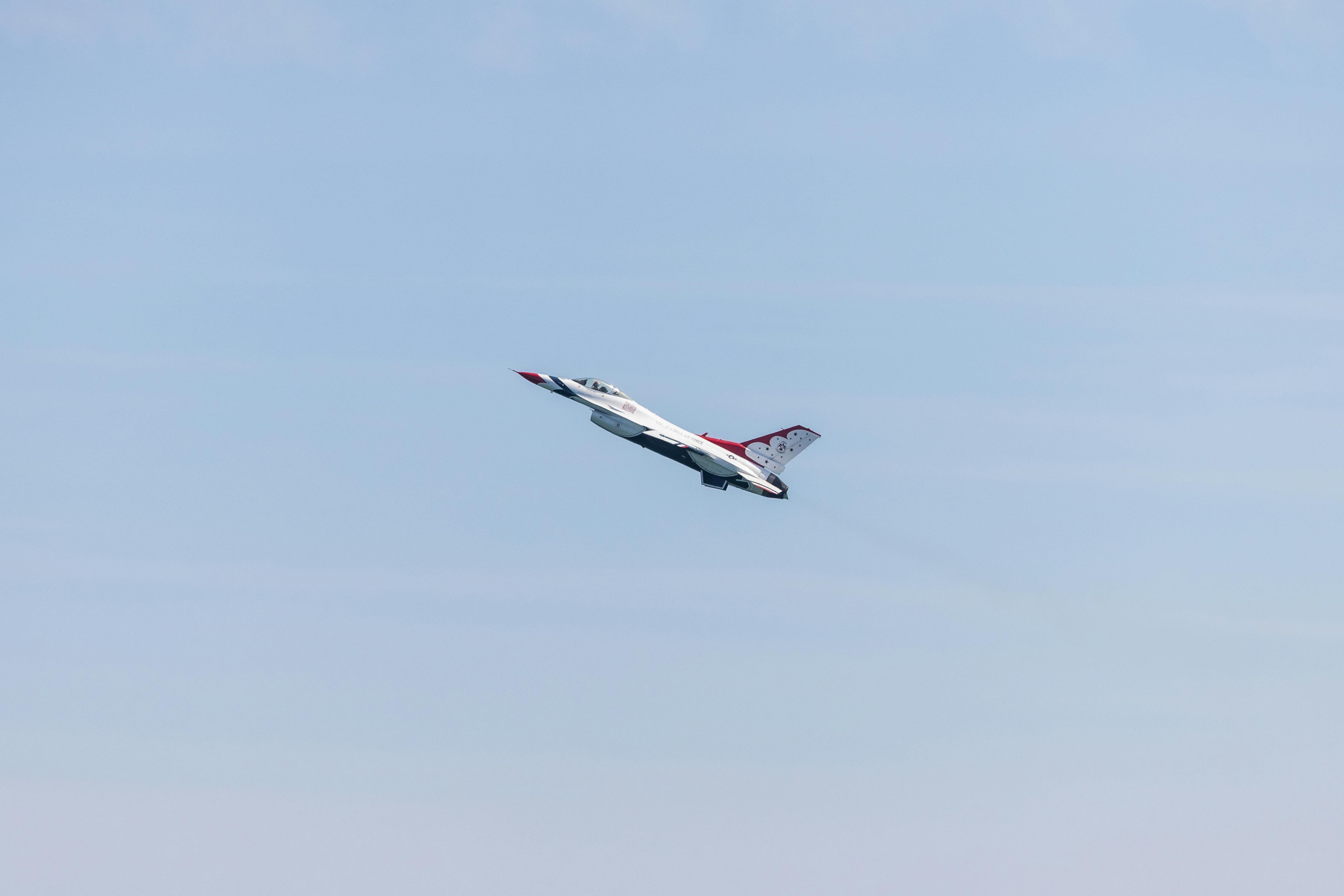 An F-16 jet from the U.S. Air Force Thunderbirds flying during an airshow in a clear blue sky.