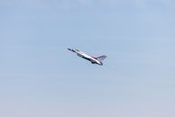 An F-16 jet from the U.S. Air Force Thunderbirds flying during an airshow in a clear blue sky.