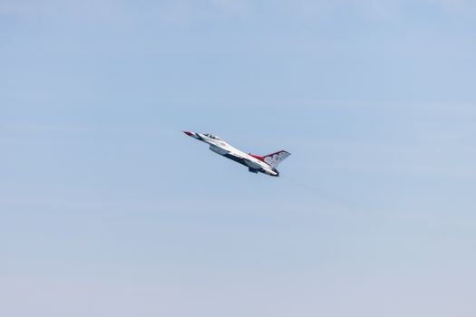 An F-16 jet from the U.S. Air Force Thunderbirds flying during an airshow in a clear blue sky.