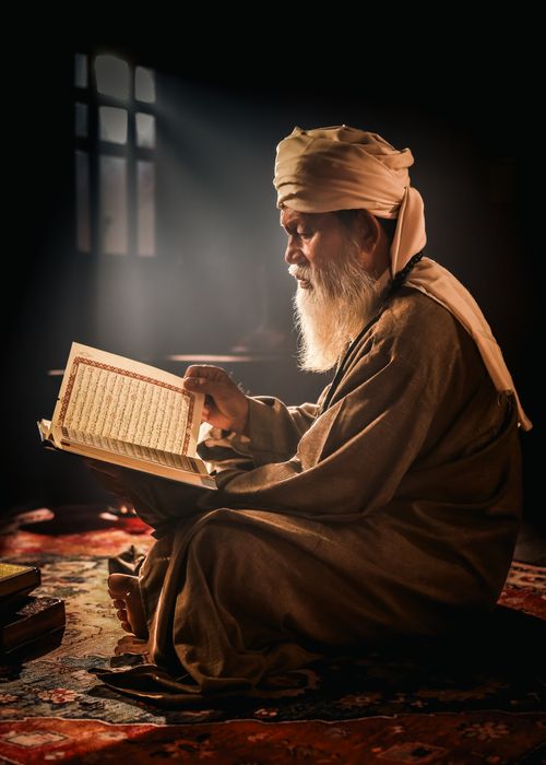 Free An elderly man intently reads a holy book by a window, highlighted by warm, natural light. Stock Photo