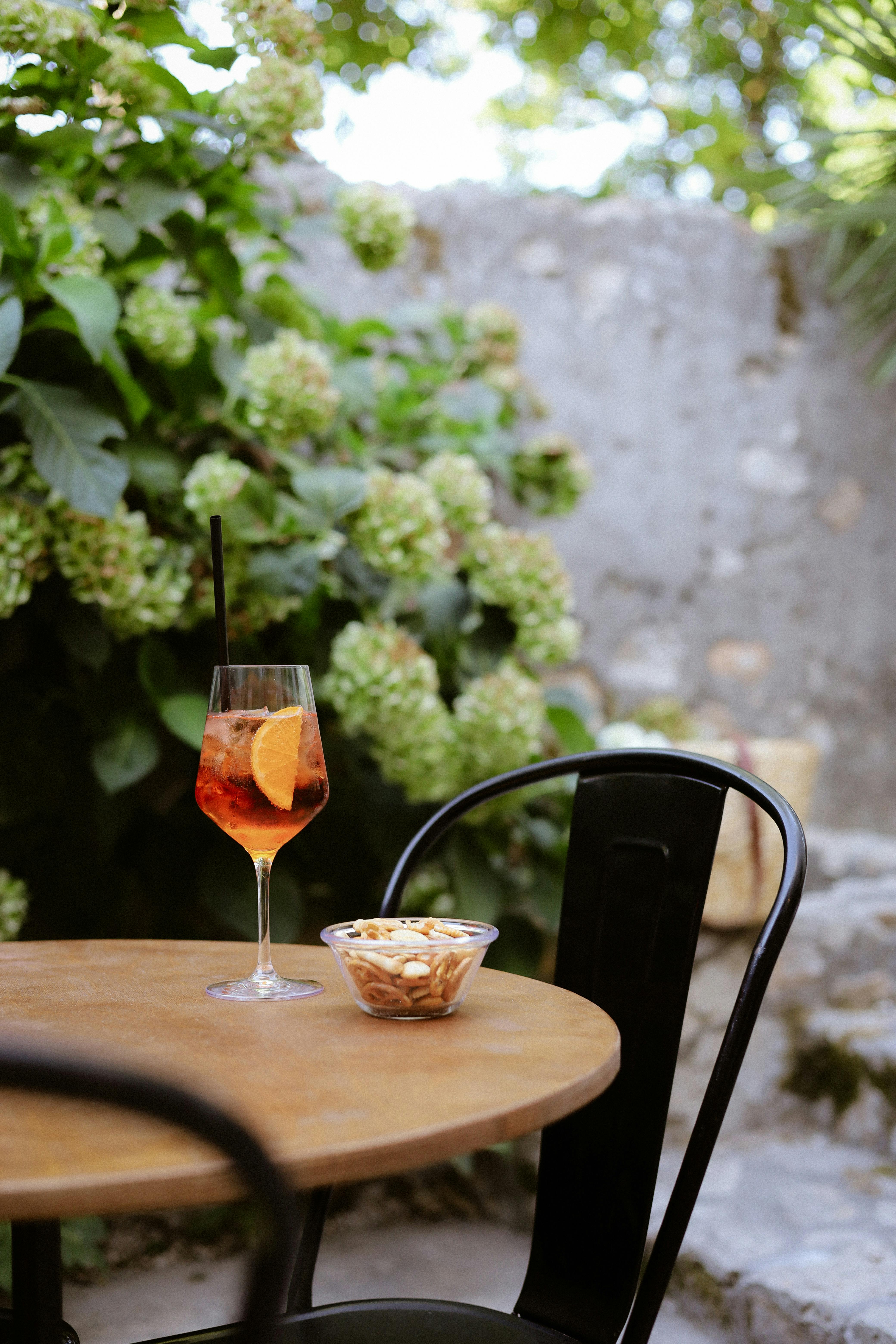 A refreshing Aperol Spritz with nuts on a charming Italian patio setting amidst lush greenery.
