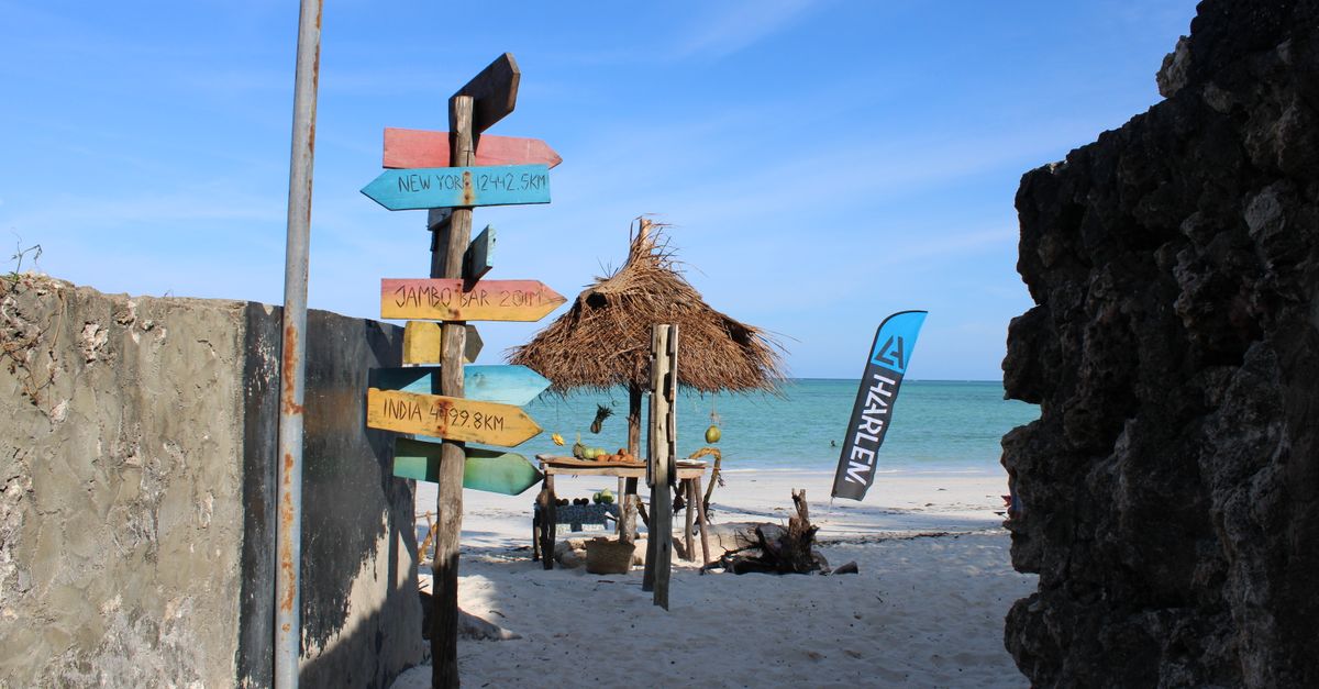 A vibrant signpost and straw hut on the sandy shores of Paje Beach, Tanzania.