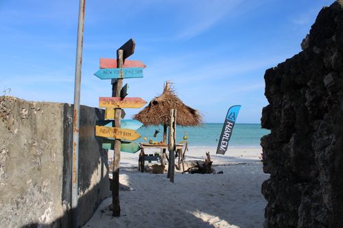 Free A vibrant signpost and straw hut on the sandy shores of Paje Beach, Tanzania. Stock Photo
