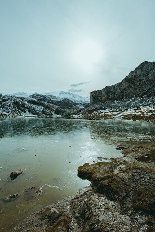 Breathtaking scenery of peaceful pond surrounded by snowy rocky formations and reflecting mountains slopes on sunny winter day