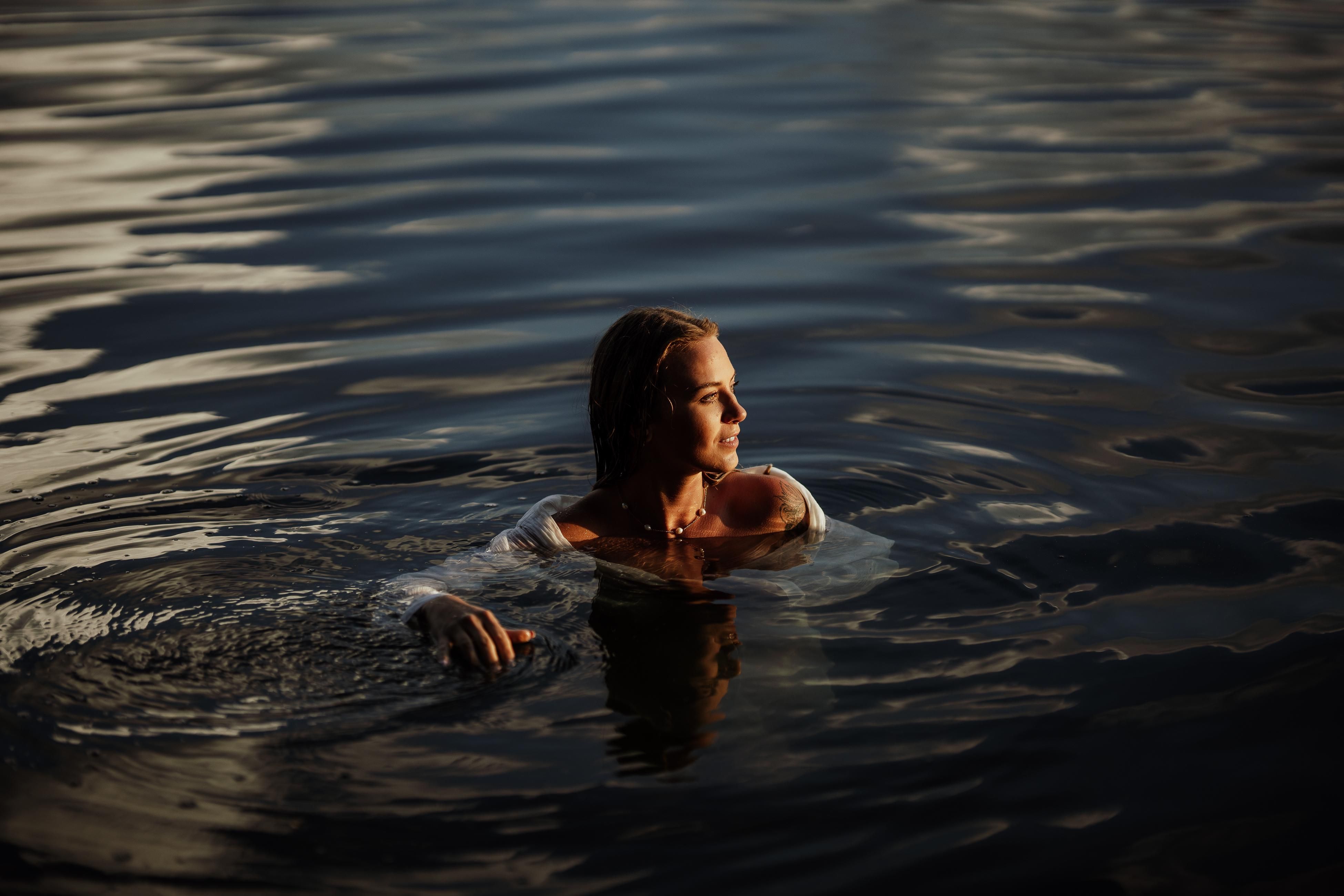 Serene scene of a woman swimming in calm waters during sunset, reflecting peace.