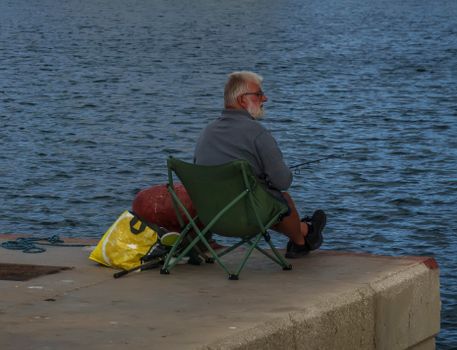 Elderly man fishing by the waterfront in Calpe, Spain, capturing a peaceful outdoor moment.