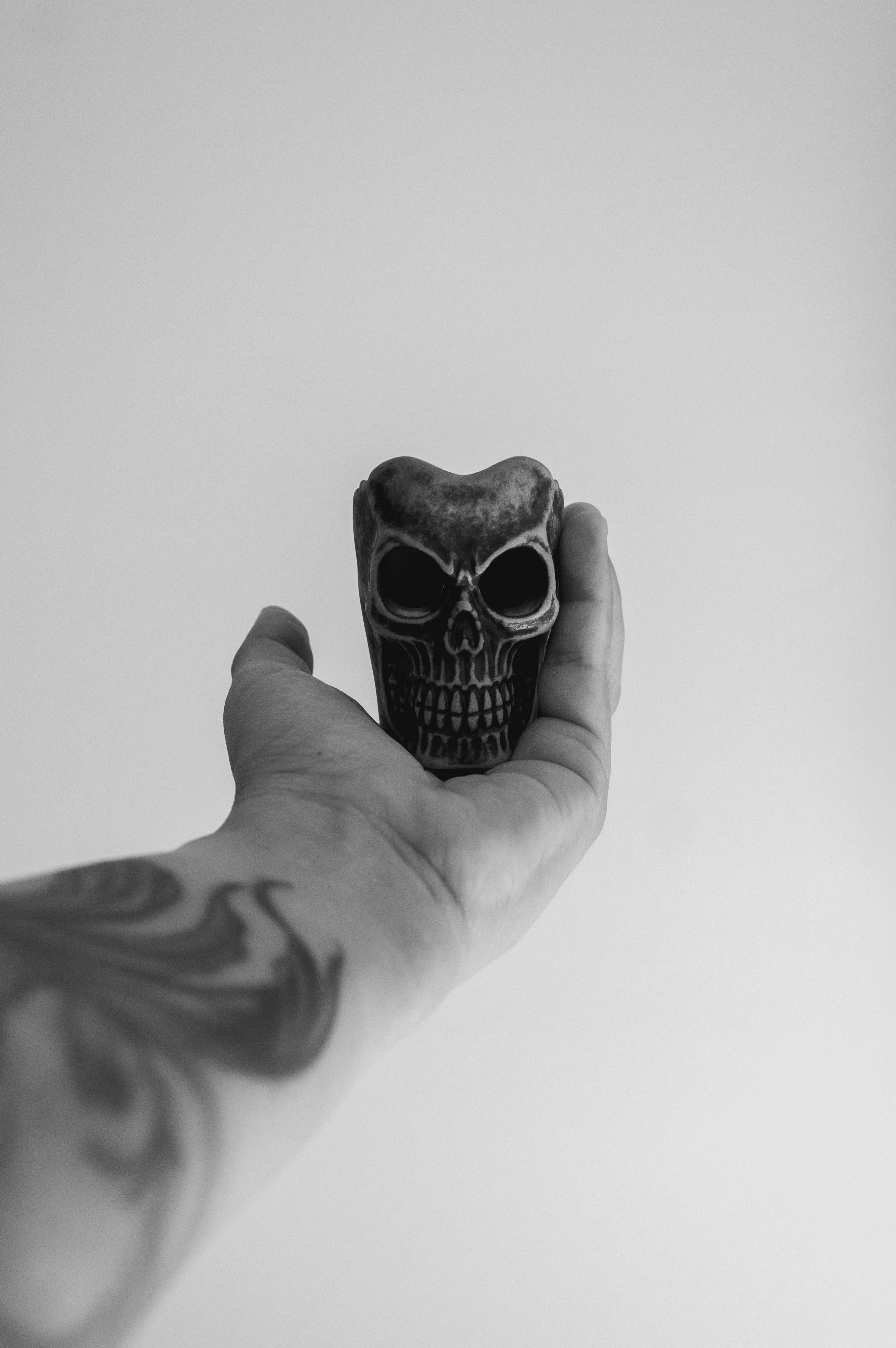 Gratis Una mano tatuata regge una scultura a forma di teschio in un ambiente in bianco e nero, che trasmette un'atmosfera gotica. Foto a disposizione
