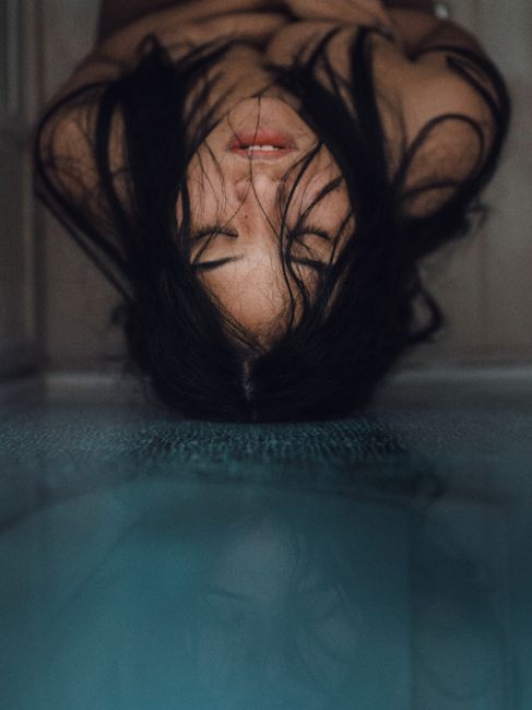 A striking portrait of a woman with long hair and a serene expression, reflected on a smooth surface.