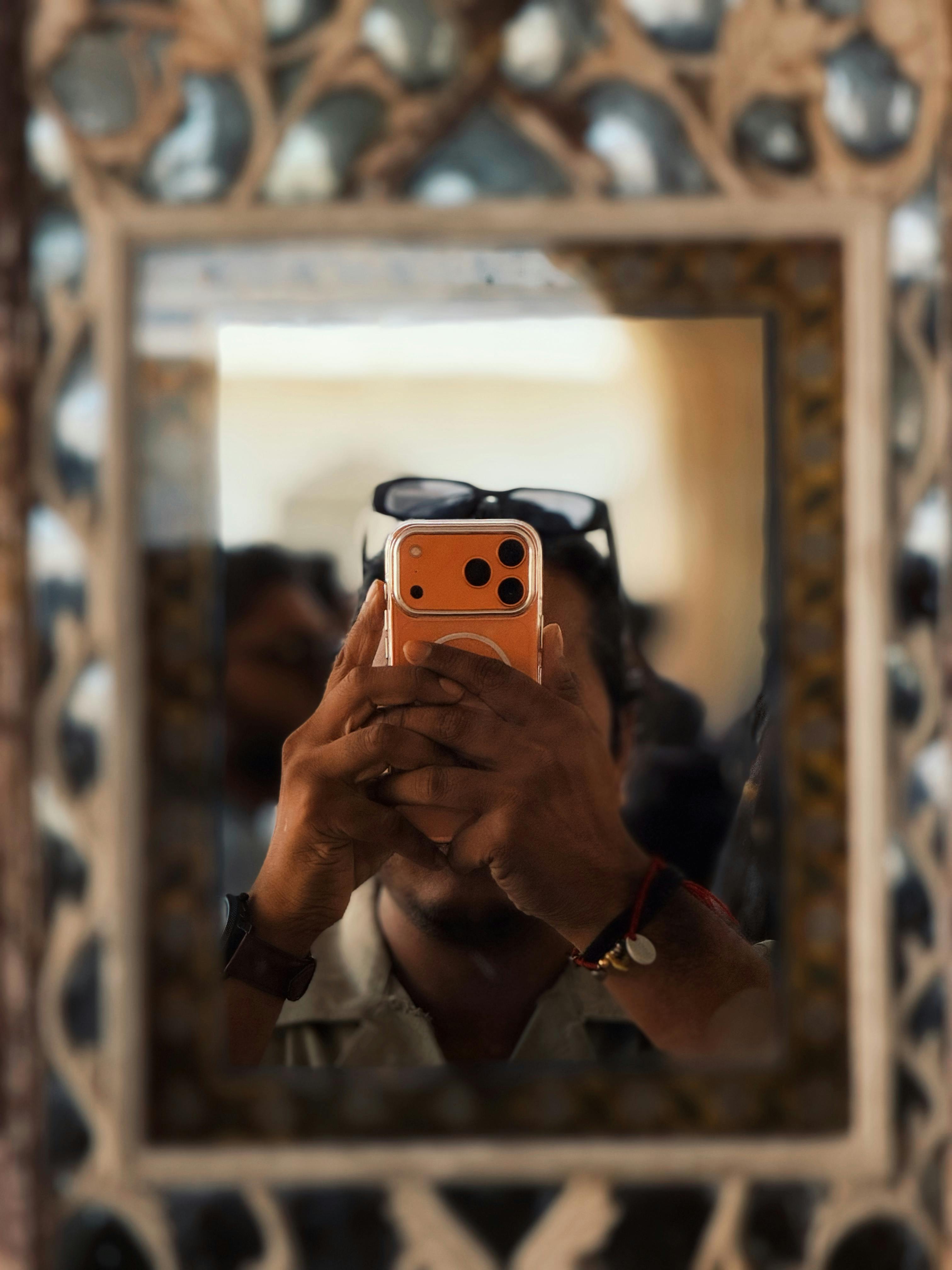 Gratis Mand tager en spejlselfie med en smartphone i en udsmykket ramme, der fremviser et indviklet design. Lagerfoto