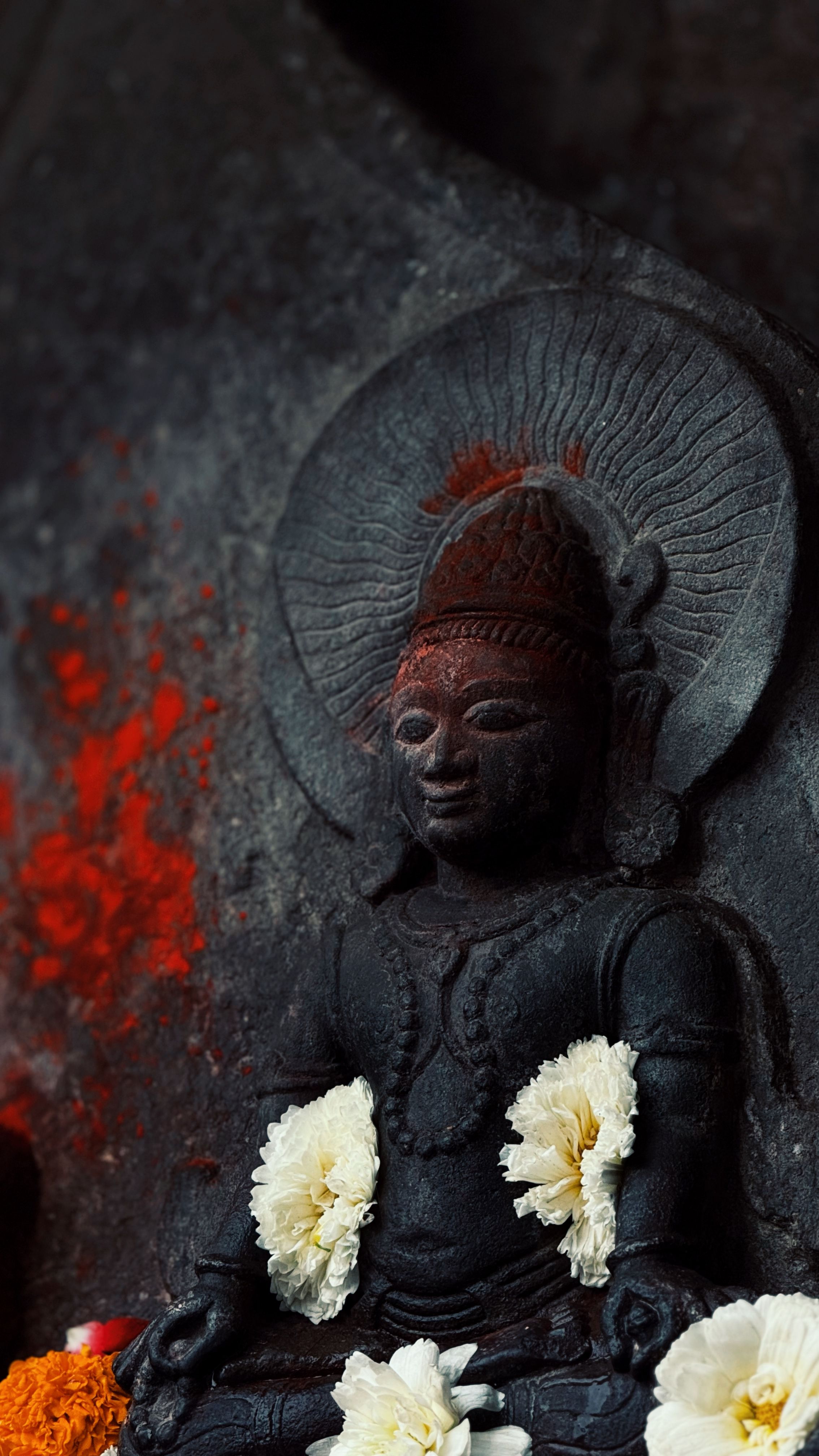 A detailed view of an ancient Hindu statue adorned with white flowers, set against a textured background.