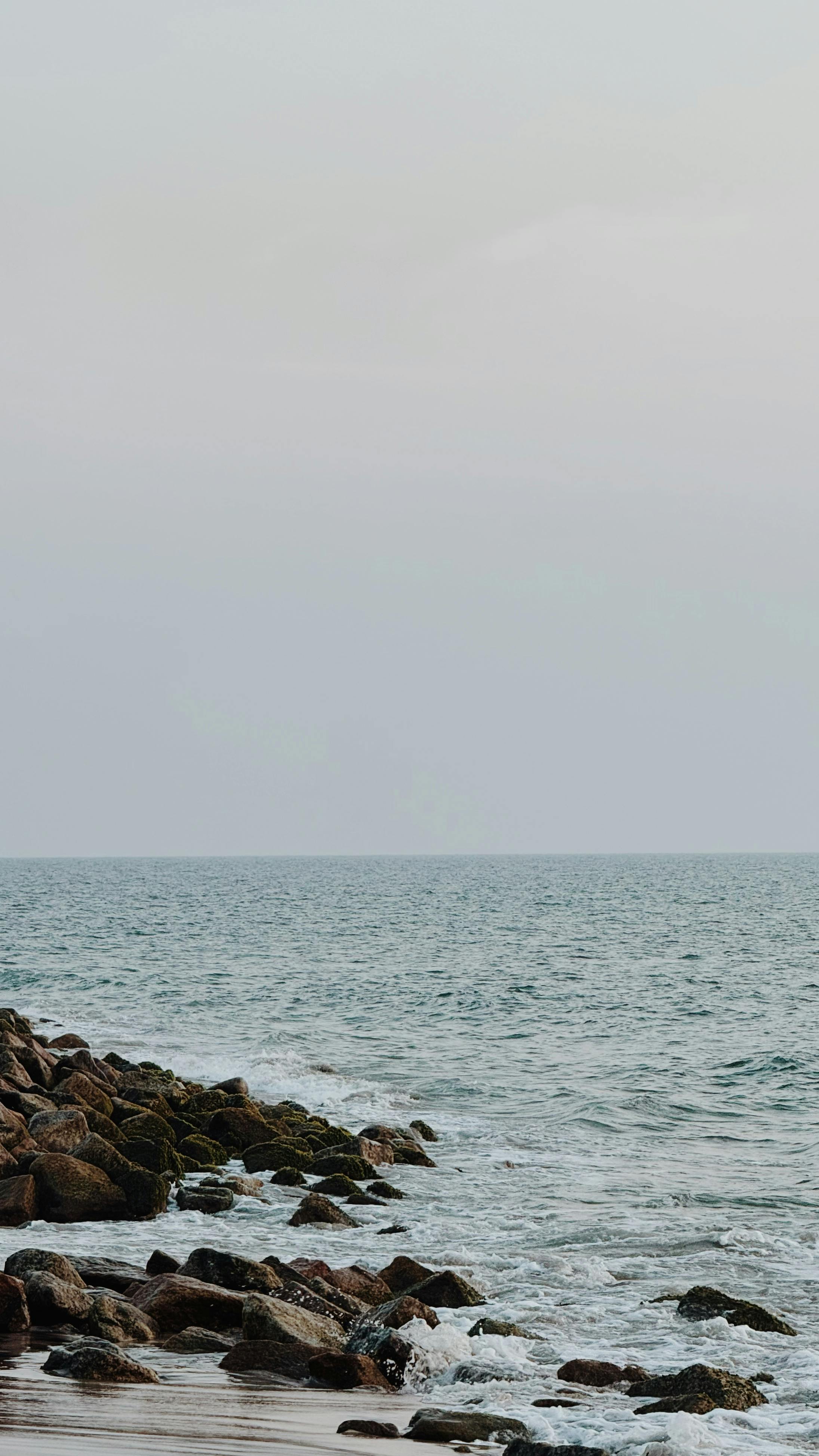 Ücretsiz Bulutlu gökyüzü altında kayalık kıyı şeridinin sakin denizle buluştuğu huzurlu bir manzara. Stok Fotoğraflar