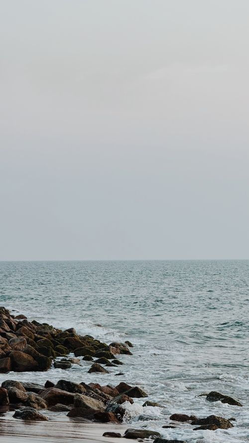 Free Peaceful scene of rocky shoreline meeting the calm sea under overcast skies. Stock Photo