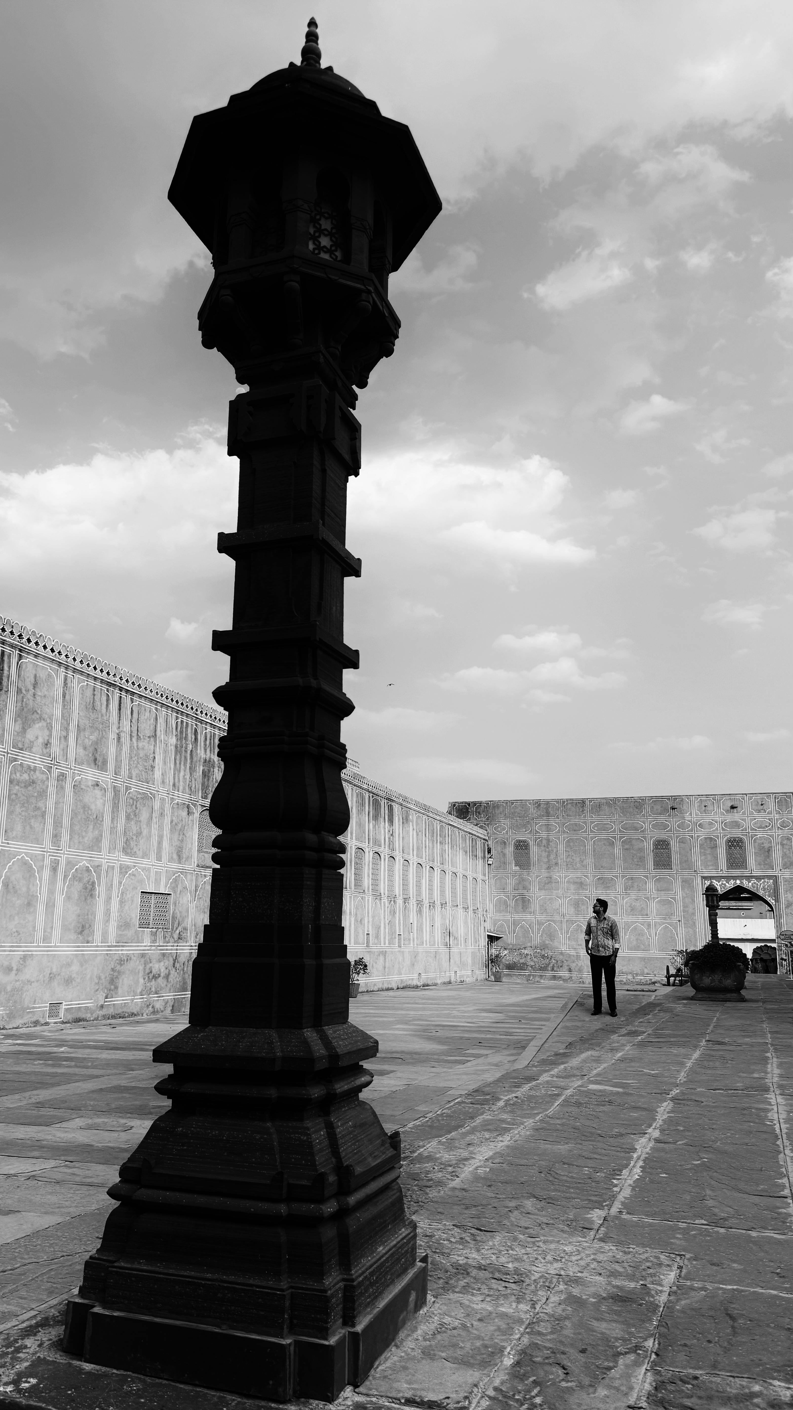 Black and white view of Amber Fort in Jaipur with a lone person walking by an ornate column.