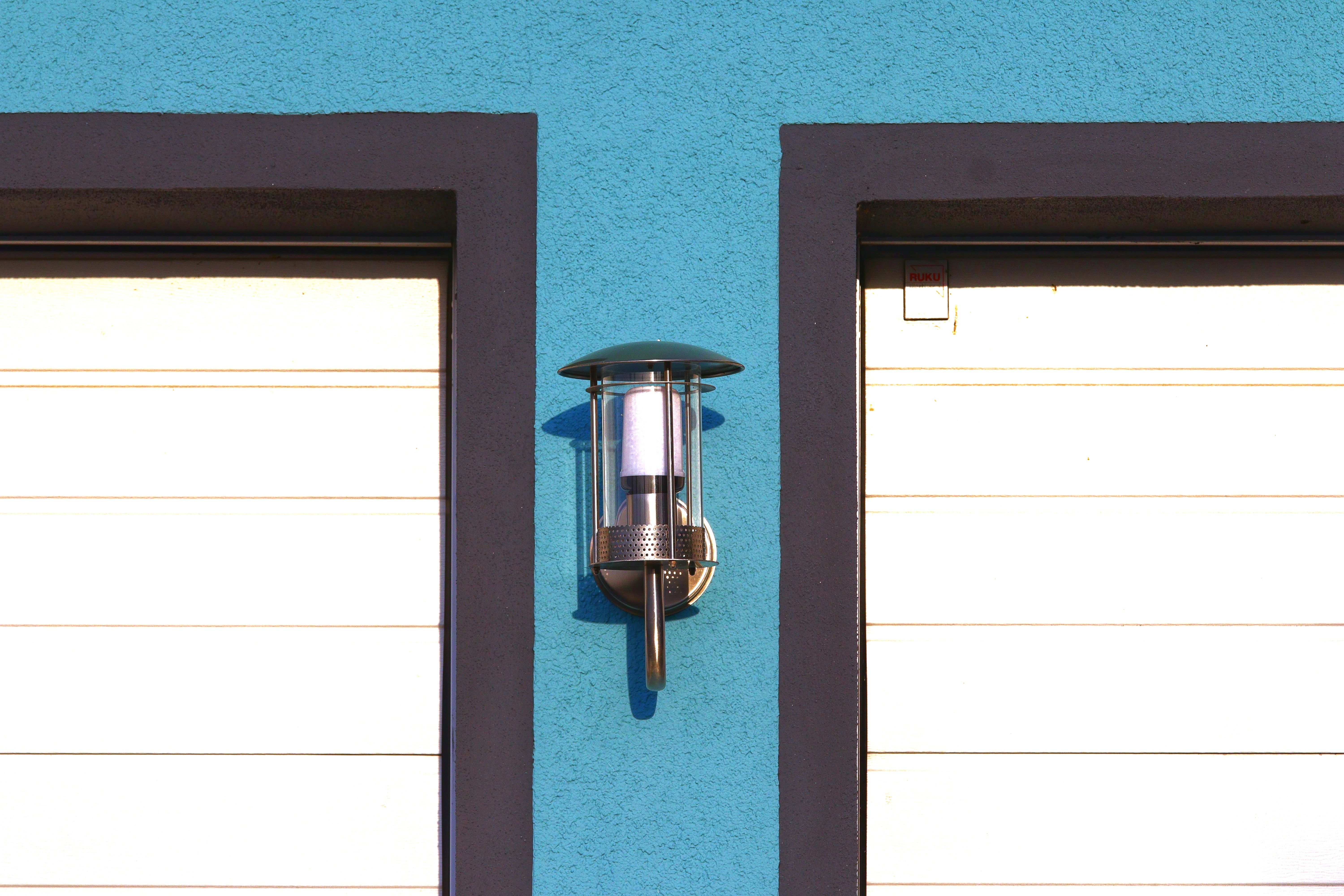 Modern outdoor wall light fixture on vibrant blue facade with contrasting black and white elements.