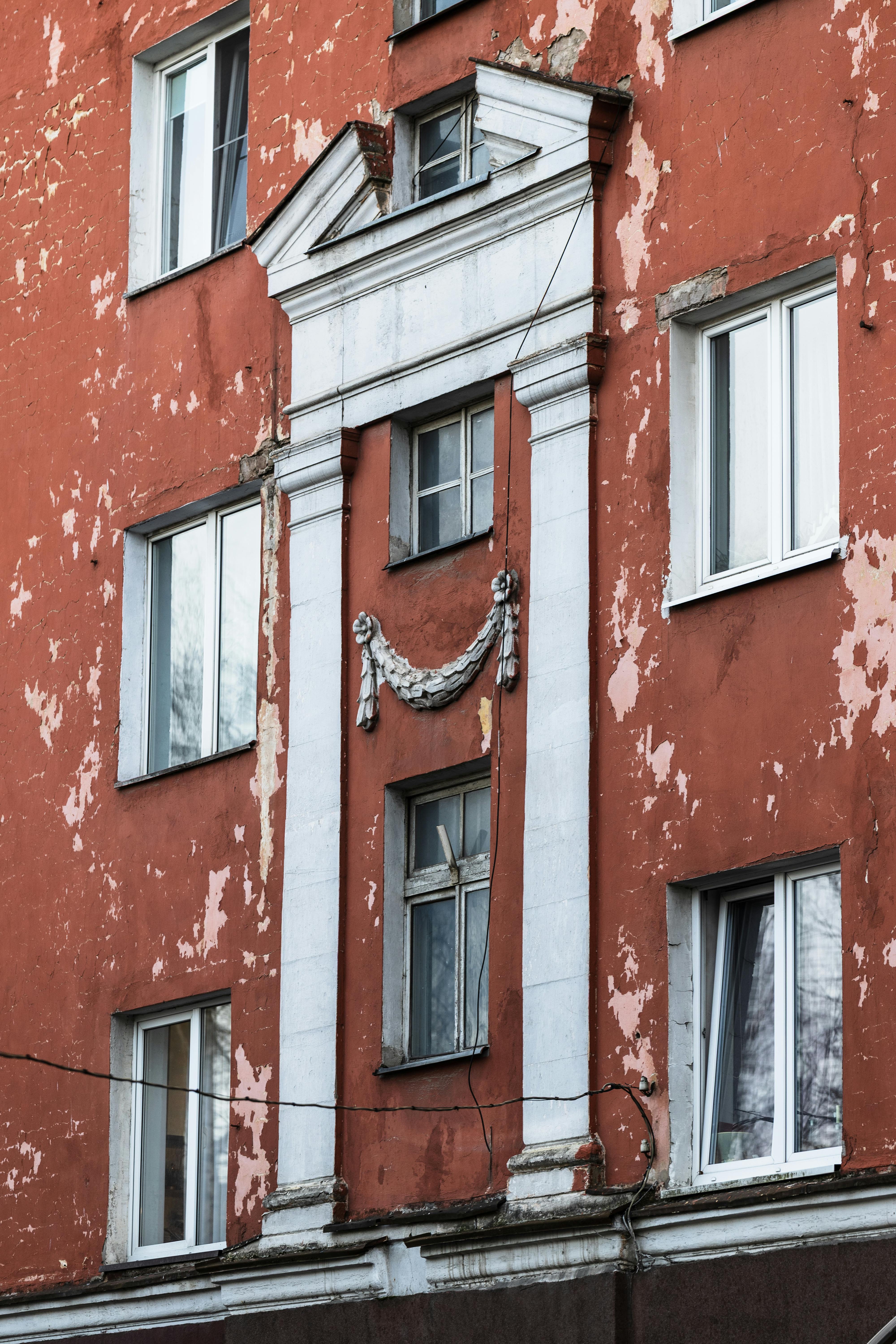 Kostenlos Nahaufnahme einer verwitterten roten Gebäudefassade mit klassischen architektonischen Details und abblätternder Farbe. Stock-Foto