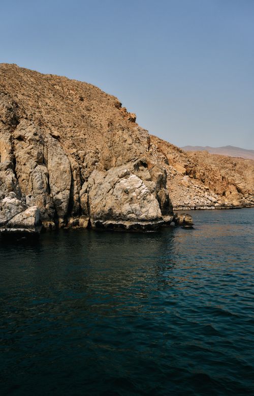 Free Breathtaking view of Musandam's rocky cliffs meeting calm sea under a clear sky. Stock Photo