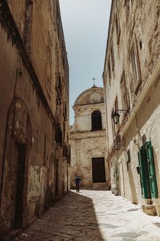 Sunlit cobblestone alley leading to a historic church in Monopoli, Italy.