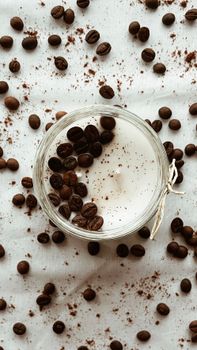 Top view of coffee beans artfully scattered on white fabric with a jar filled with frothy drink.