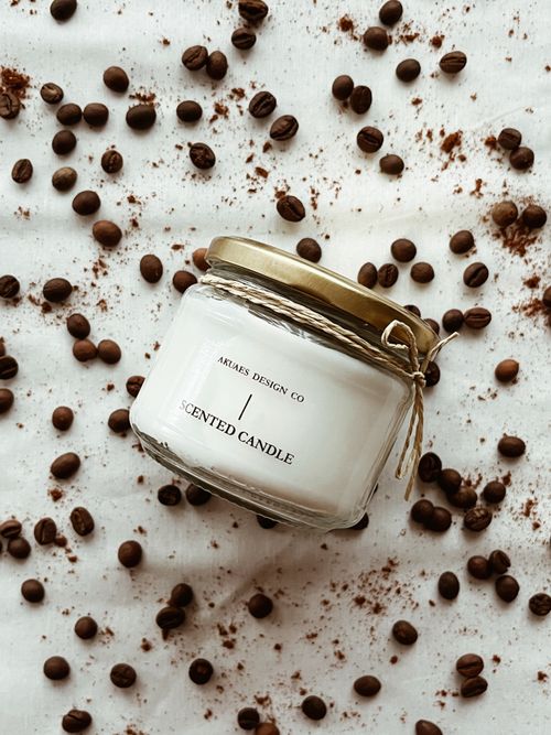Free Glass jar scented candle surrounded by coffee beans on white fabric. Stock Photo