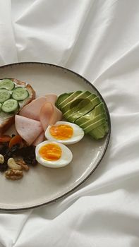 A balanced breakfast platter featuring avocado, boiled eggs, ham, and cucumber slices.