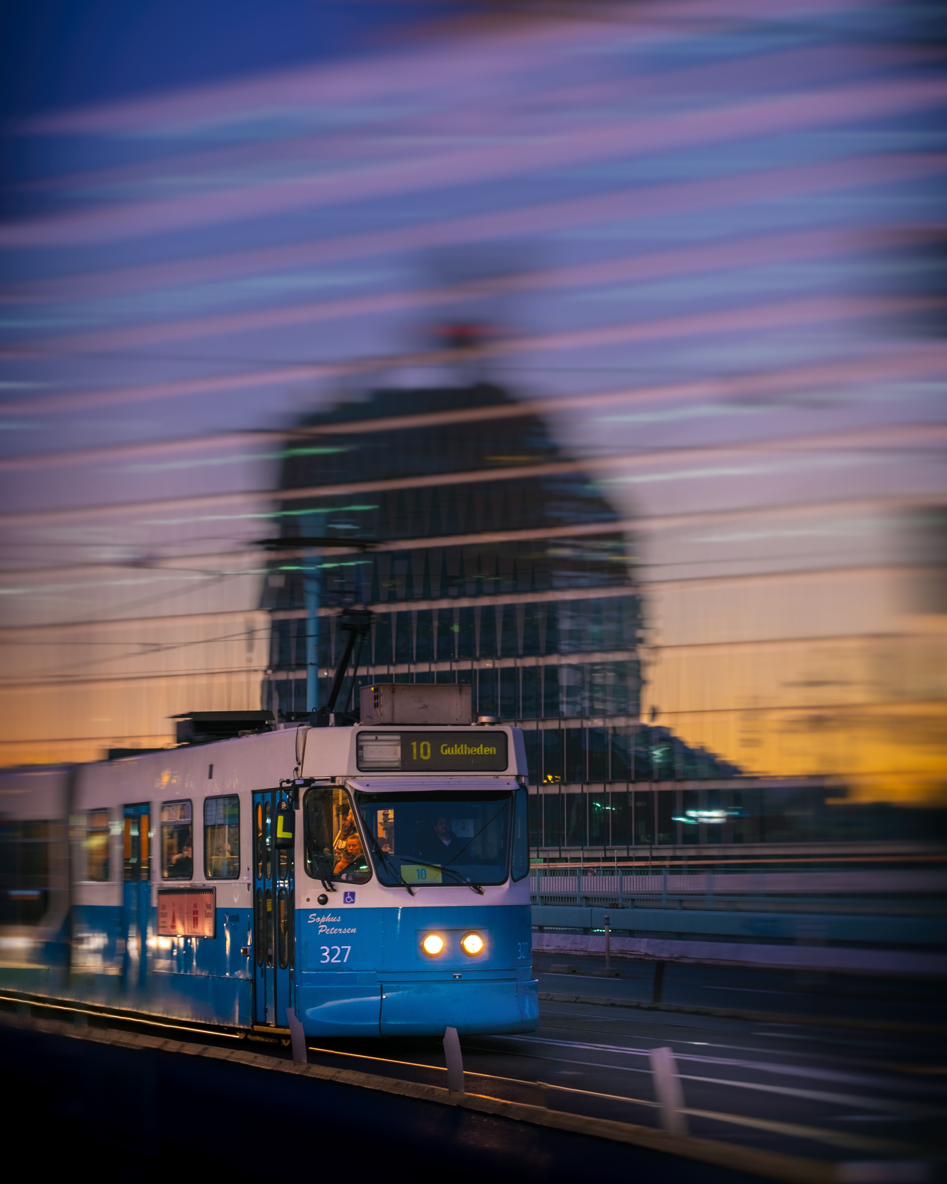 A blue tram crosses a bridge in Gothenburg at twilight, reflecting urban lights.