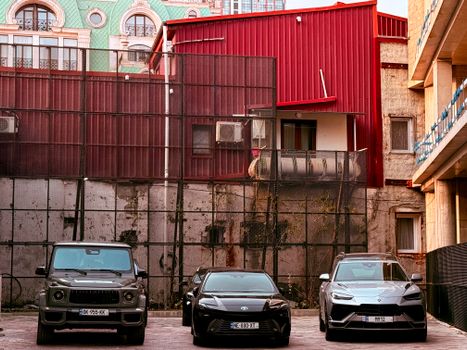 Three cars parked in an urban area with a red building and decorative architecture in the background.