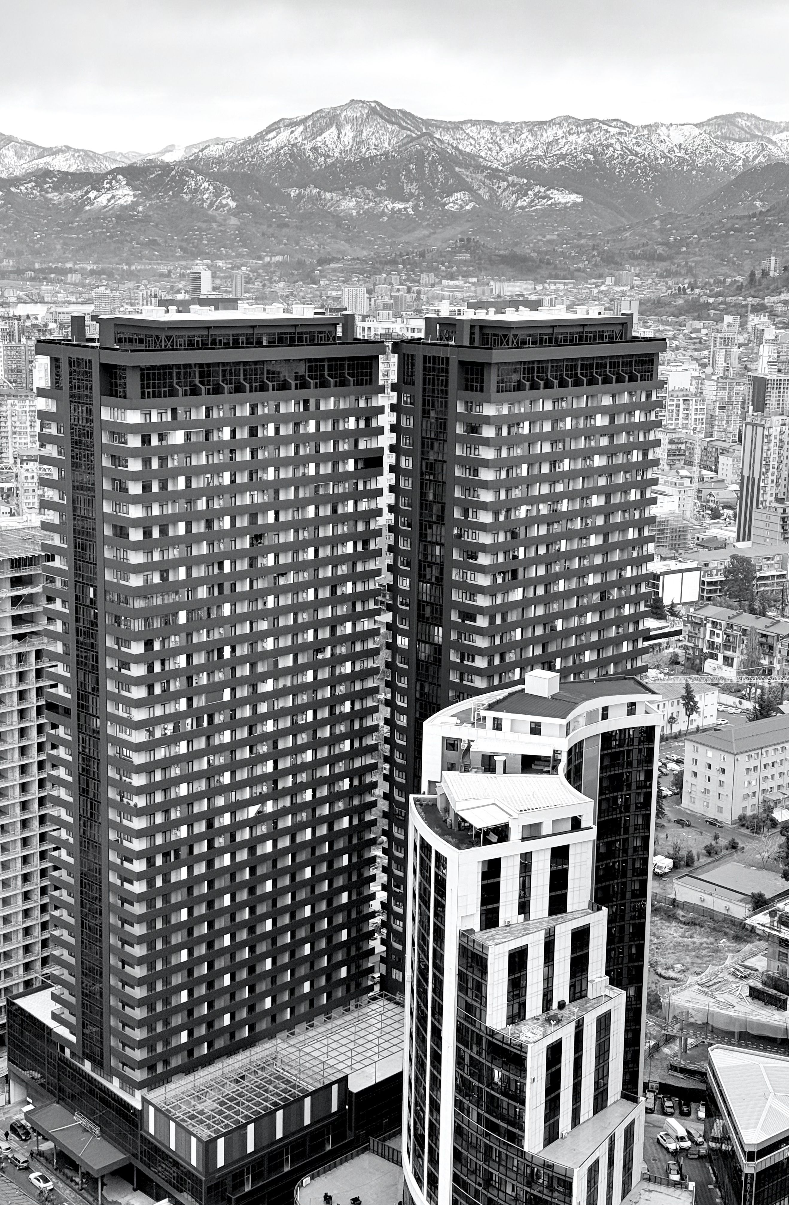 Black and white aerial photo of a modern skyline with high-rise buildings against a mountainous background.