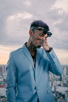 Stylish man with tattoos in blue suit against city skyline at sunset for modern urban style.