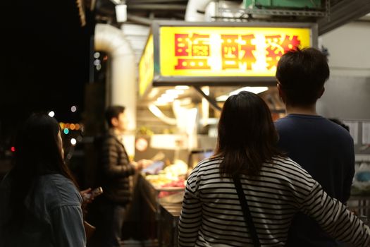 Customers waiting at a street food stand at night, vibrant atmosphere.