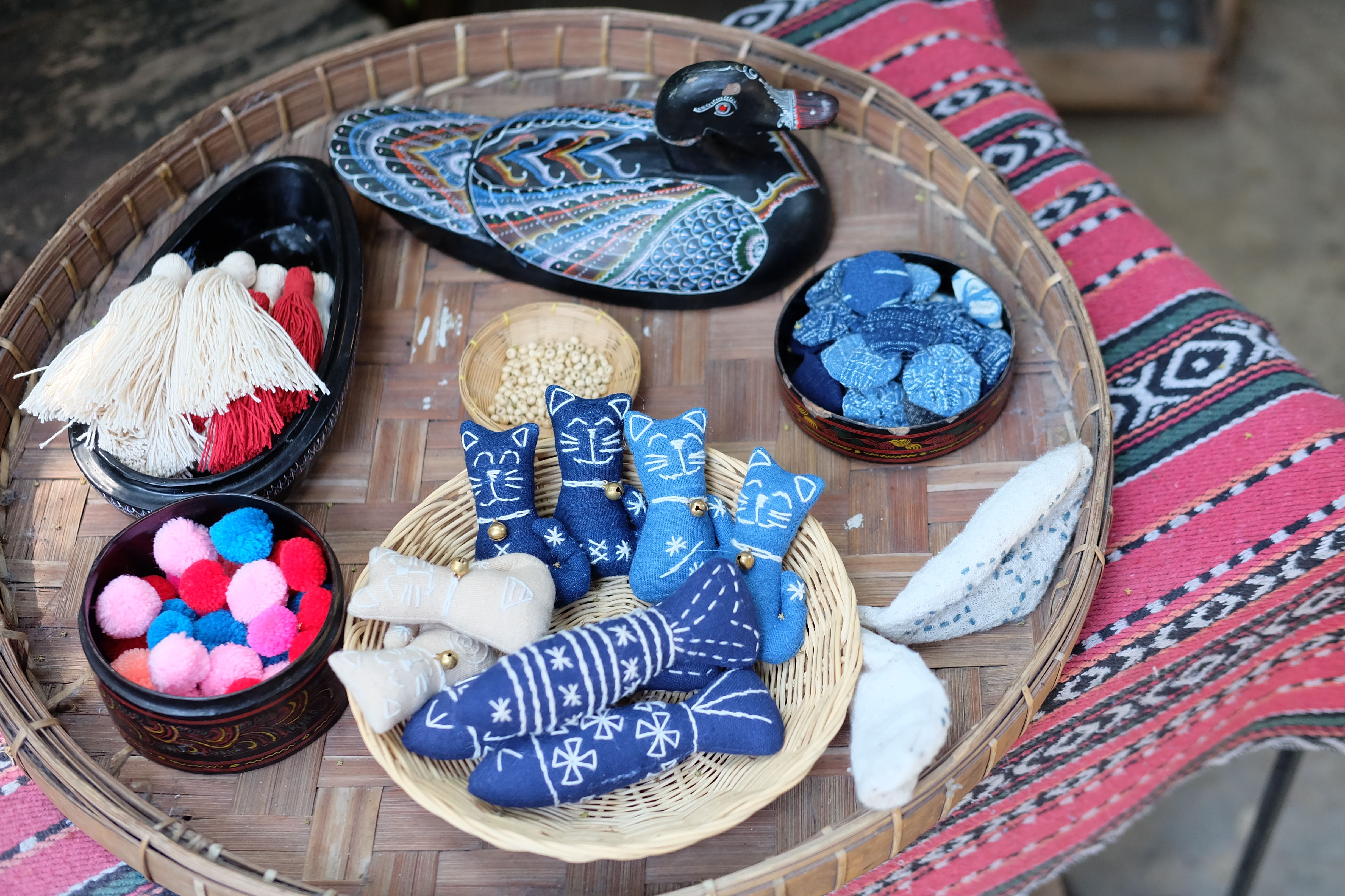 A variety of colorful handmade crafts displayed in a bamboo basket on a textile background.