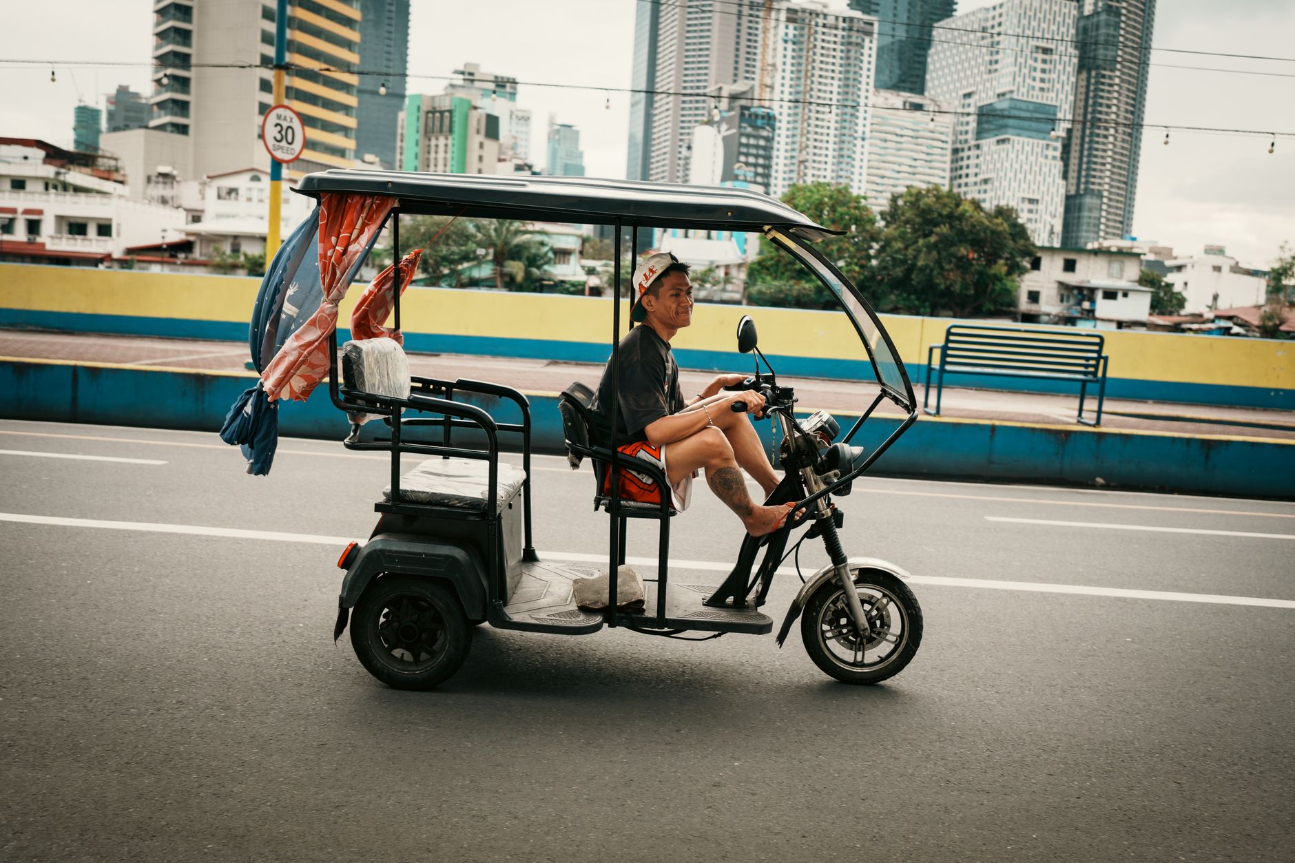 Man riding an electric tricycle on the street in Mandaluyong, with skyscrapers in the background.