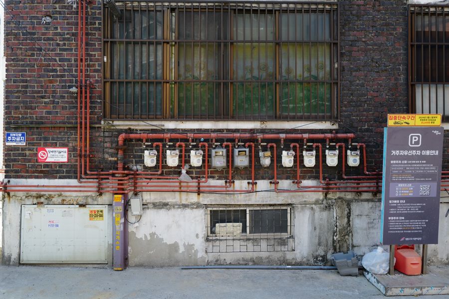 Bricked wall with gas meters and assorted signage in an urban alleyway.