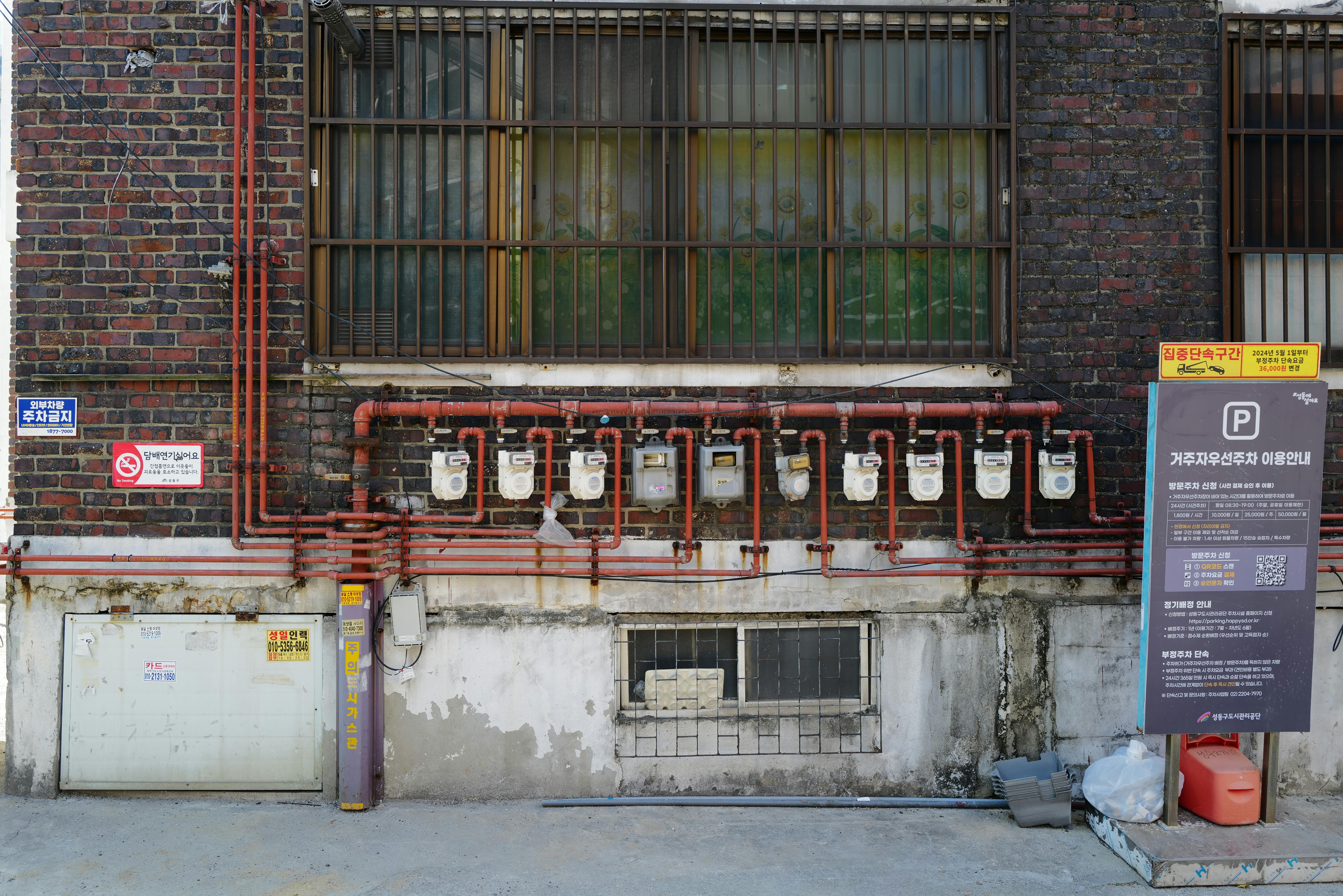 Kostenlos Eine Backsteinmauer mit Gaszählern und verschiedenen Schildern in einer städtischen Gasse. Stock-Foto