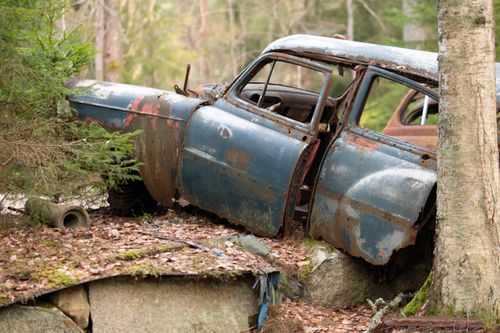 Free A rusted vintage car in a forest setting, symbolizing decay and nostalgia. Stock Photo