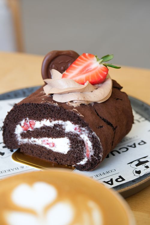Free A close-up of a chocolate Swiss roll topped with strawberry on a rustic plate. Stock Photo