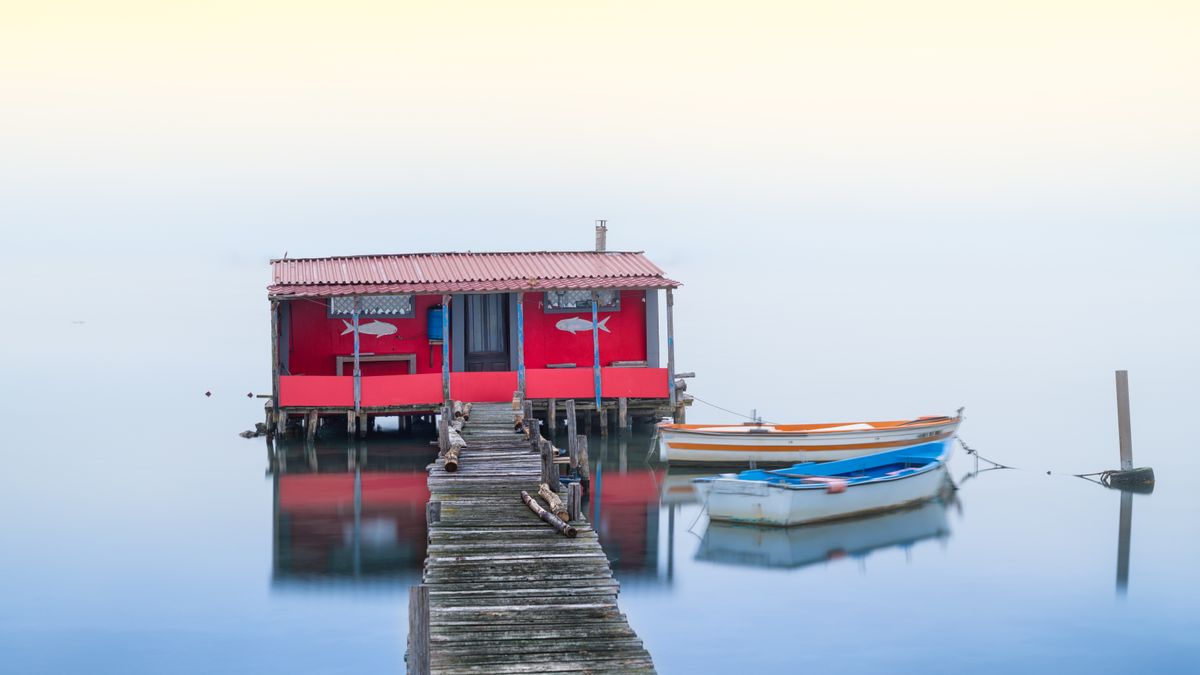 Red boathouse and moored boats on a calm lake at sunset
