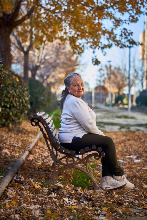 Free Senior woman sitting on park bench surrounded by fall leaves in San Sebastián de los Reyes. Stock Photo