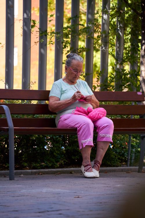 Free Senior woman knitting pink yarn outdoors on a park bench in Madrid. Stock Photo