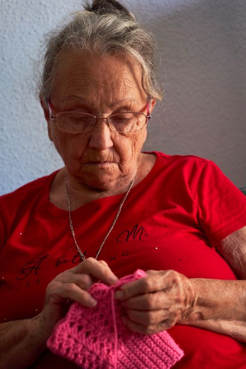 Free Senior woman knitting with pink yarn, showcasing traditional craft techniques. Stock Photo