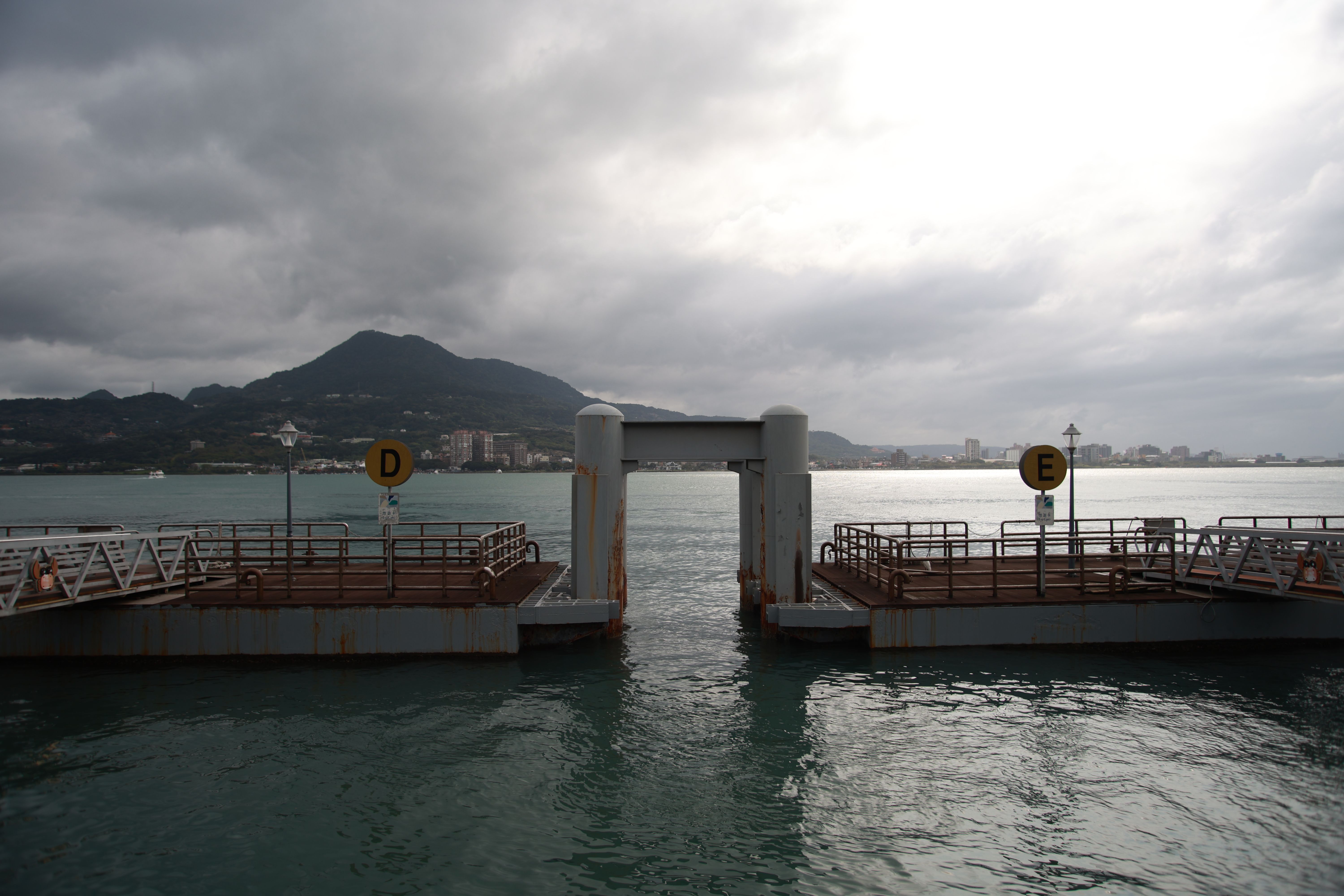 A scenic view of a pier with mountains in the background under a cloudy sky.
